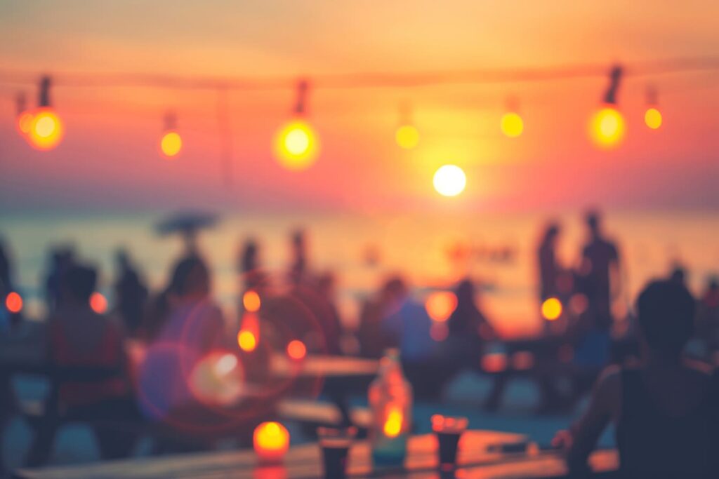 Gruppe von Mitarbeitern genießt eine Firmenfeier am Strand mit aufgehängten Lichtern und einem atemberaubenden Sonnenuntergang im Hintergrund in NRW