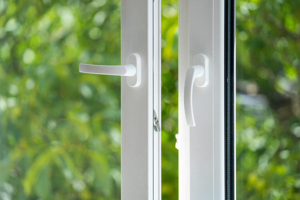 Ein modernes, weißes Fenster mit zwei Griffen, geöffnet und mit Blick auf grüne Bäume im Hintergrund. Das Fenster zeigt klare, schlichte Linien und lässt viel Licht herein, wodurch eine helle und einladende Atmosphäre entsteht.