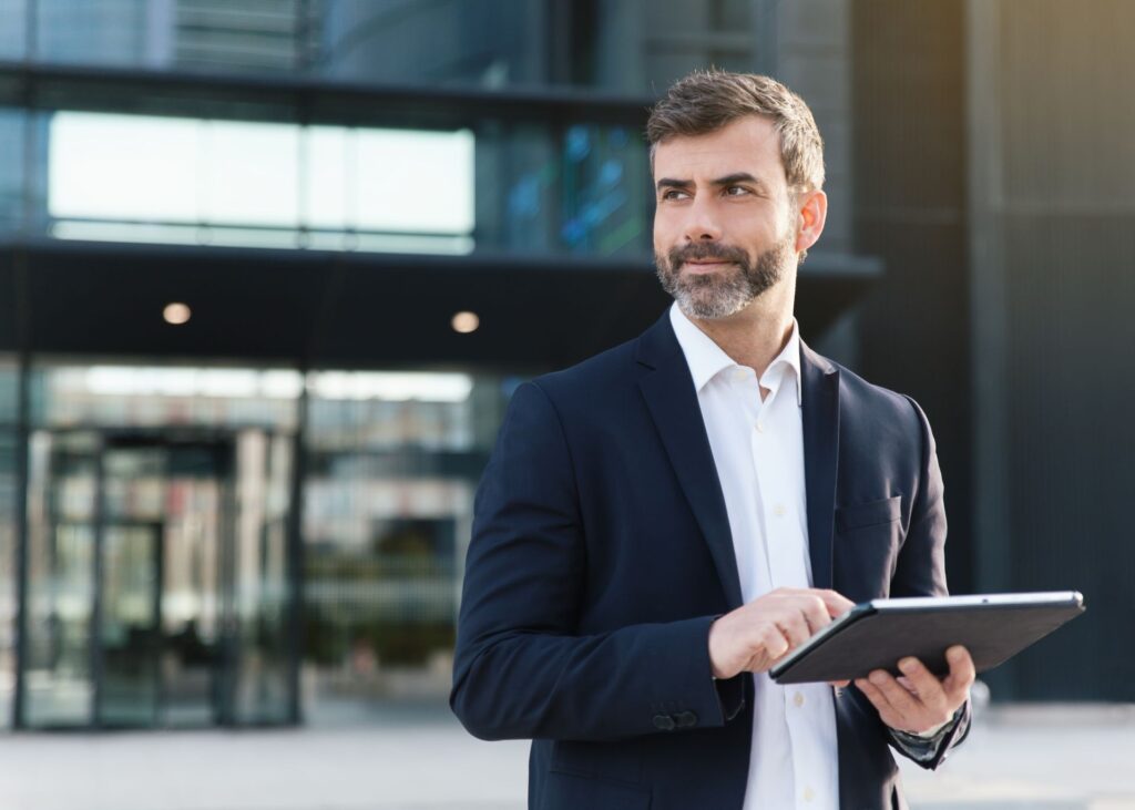 Ein selbstbewusster Unternehmer in einem modernen Business-Anzug nutzt ein Tablet, um digitale Strategien für die Optimierung seiner Geschäftsführung zu planen.