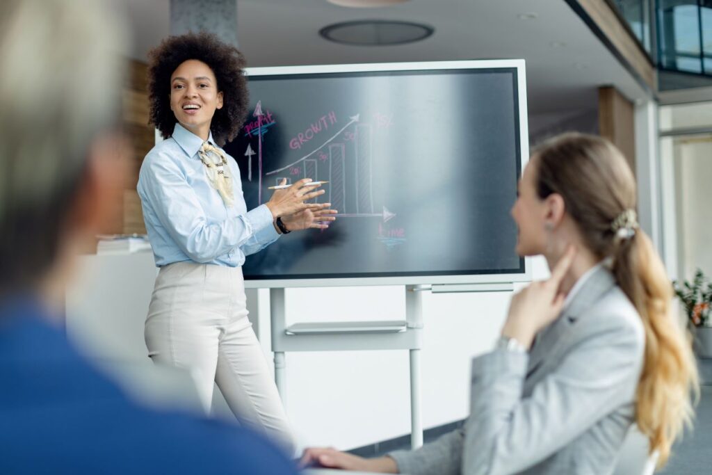 Geschäftsfrau präsentiert Wachstumsdiagramm und erklärt den Einsatz von Differenzdruckmessgeräten zur Prozessoptimierung vor Kollegen im modernen Büro.