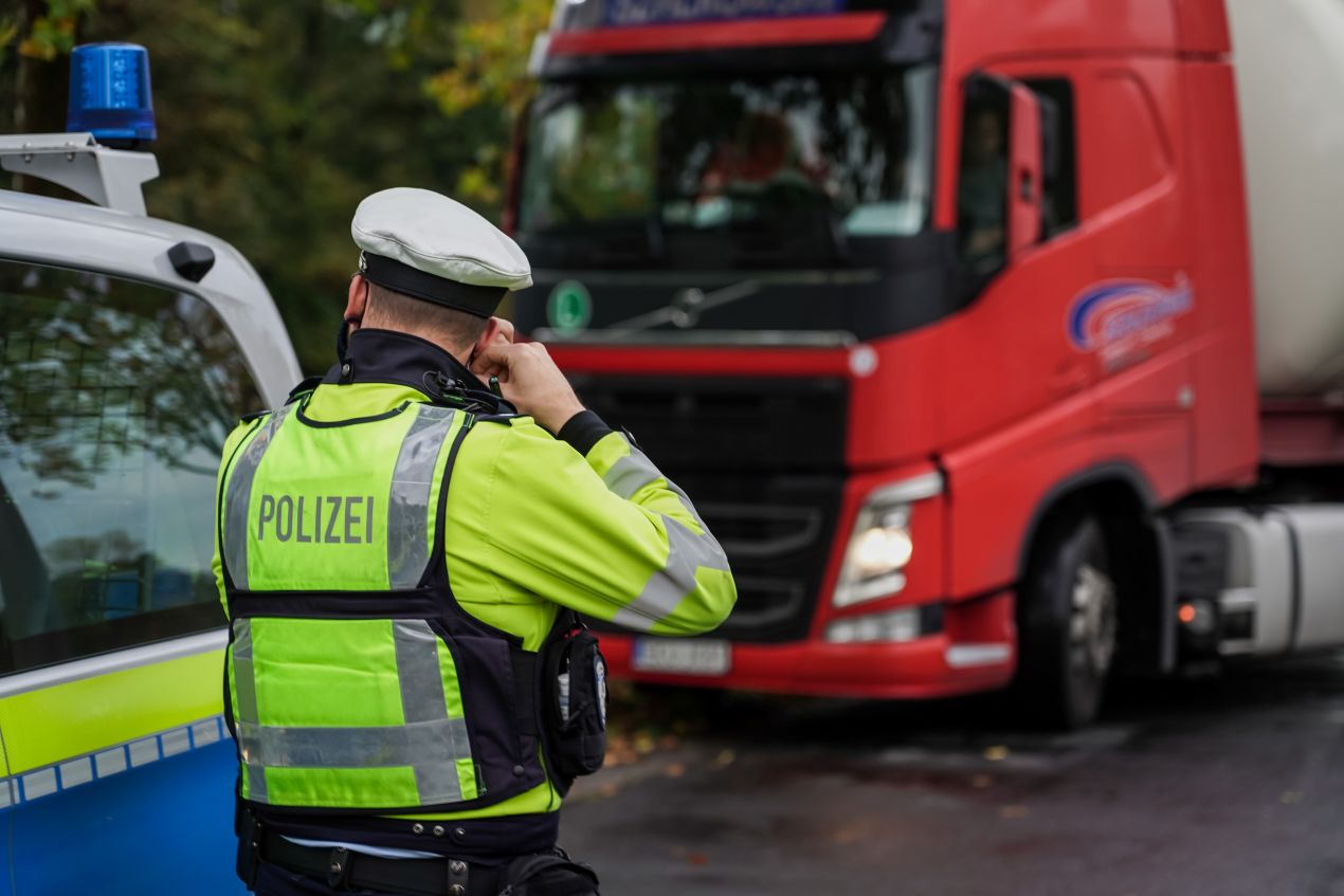 Polizist bei einer Verkehrskontrolle überprüft die Beleuchtung eines roten LKWs.