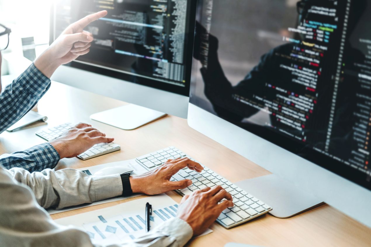 Entwicklerteam arbeitet an Code auf großen Monitoren – symbolisiert die Programmierung und Umsetzung eines Ota Updates für moderne Softwarelösungen.