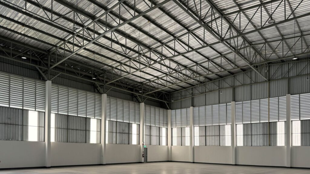 Leere Lagerhalle mit Stahltragewerk, Lichtpaneelen und glattem Boden – moderne Industriearchitektur fuer flexible Nutzung